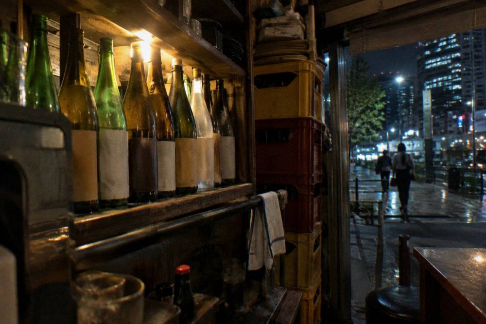 A bar shelf lined with sake bottles behind a dimly lit Tokyo counter