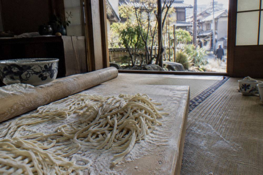 Fresh ramen noodles dusted with flour resting on a wooden board beside a rolling pin