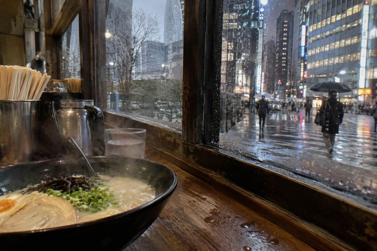 Steam rising from a bowl of tonkotsu ramen on a wooden counter beside chopsticks and a ladle