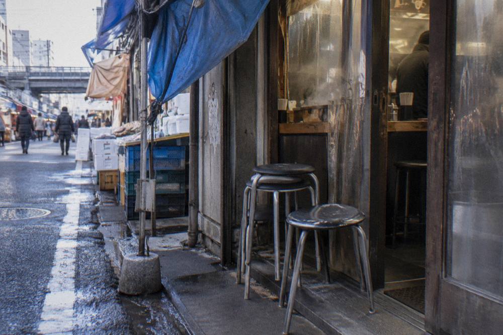 Small queue of chairs outside a narrow Tokyo noodle shop entrance in late afternoon