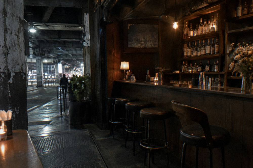 A quiet Tokyo bar interior with bottles shelved against the wall and stools at the counter