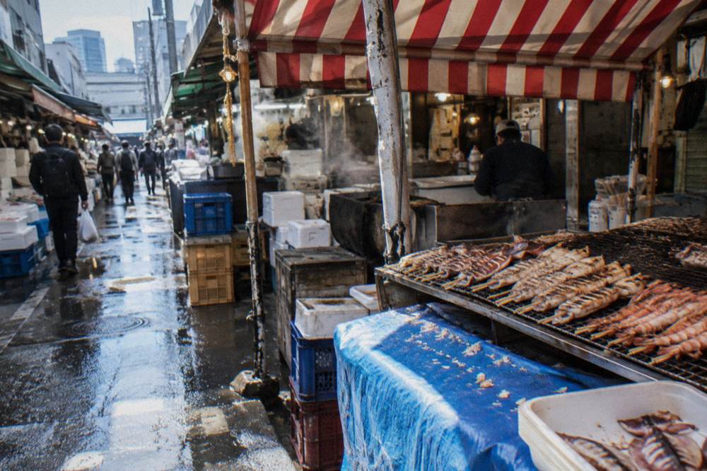 Market stall displaying grilled seafood skewers under a striped awning
