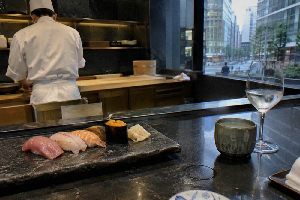 Sushi pieces arranged on a dark stone counter beside small tasting glasses