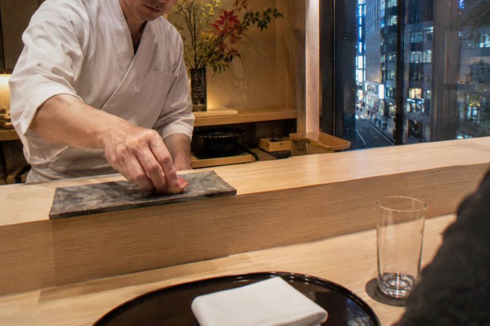 Chef placing a piece of nigiri sushi across a wooden counter