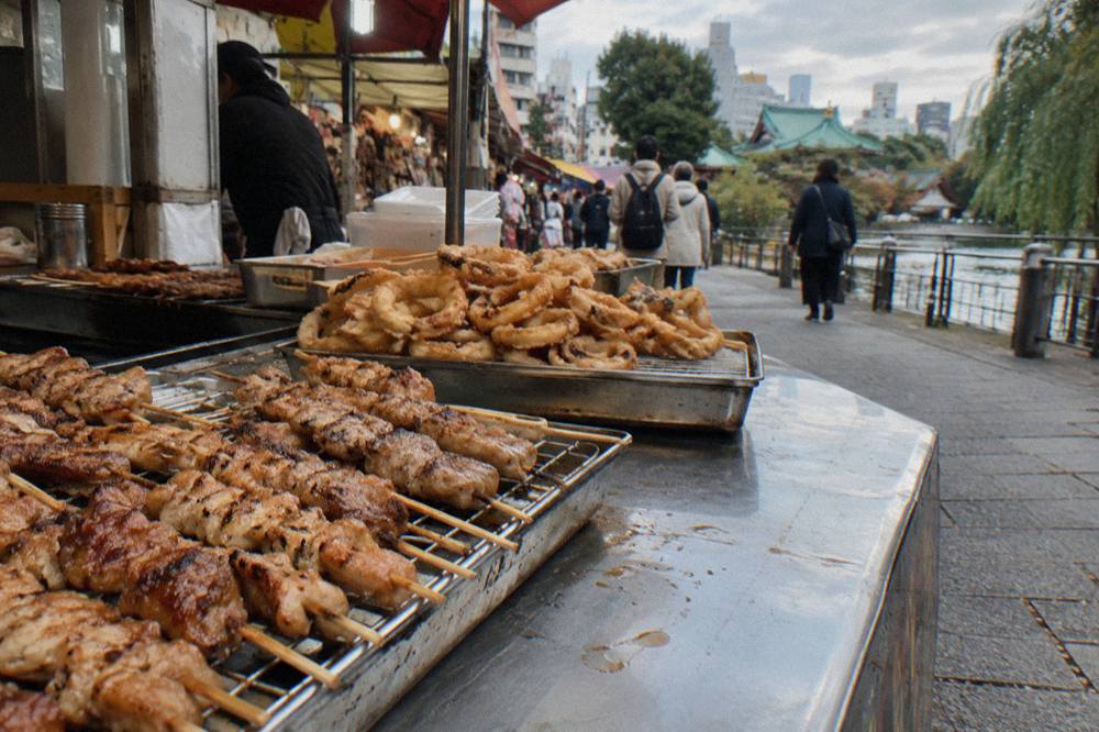 Close view of grilled skewers and fried snacks displayed at a crowded market stall counter