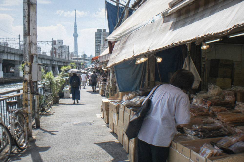 Shopper buying snack food from a stall beside stacked boxes on a busy market lane