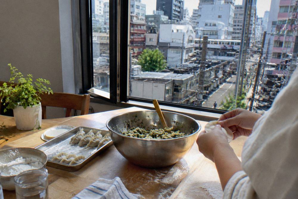 Hands folding gyoza dumplings at a wooden table in a bright kitchen