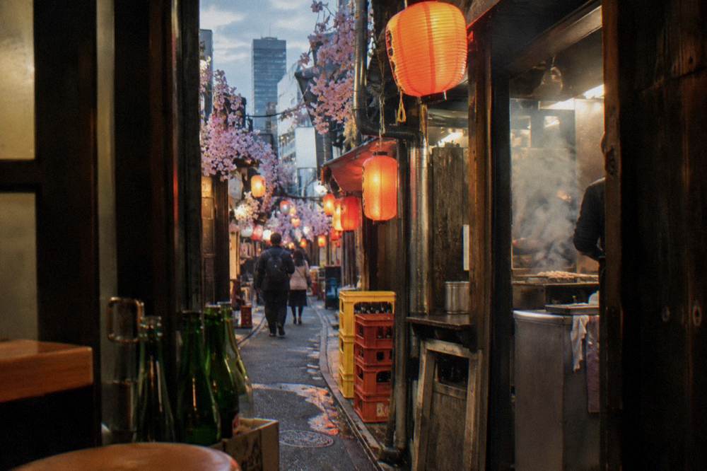 Lantern-lit food stall lane in Shinjuku at dusk with steam rising