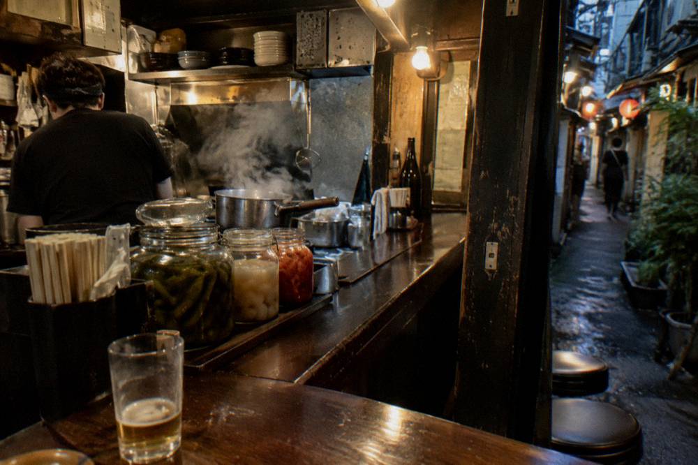 Steam rising from a small Tokyo noodle shop counter with jars of pickled vegetables