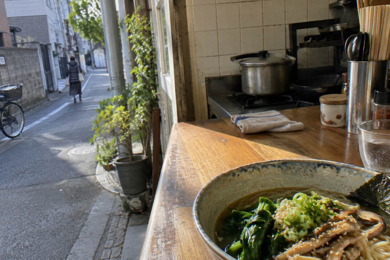 Bowl of plant-based ramen with vegetables on a wooden counter in a small Tokyo kitchen