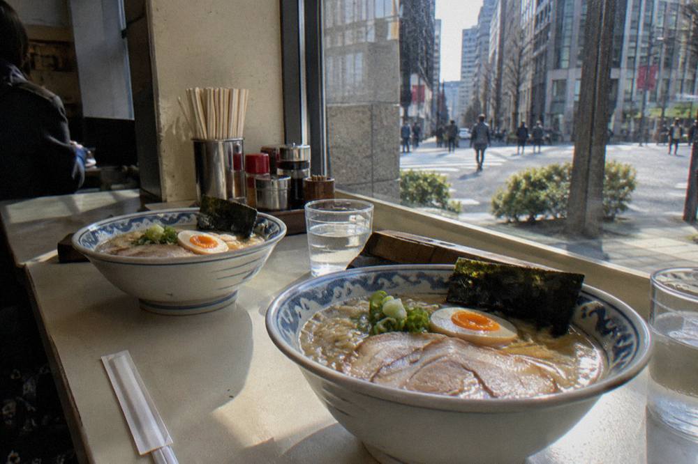 Two bowls of ramen with sliced pork, egg and nori set on a counter beside chopsticks