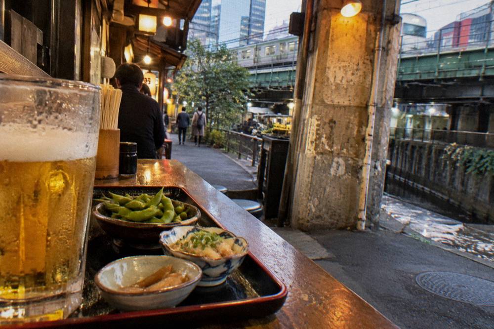 Tray of small izakaya dishes and a beer on a wooden counter