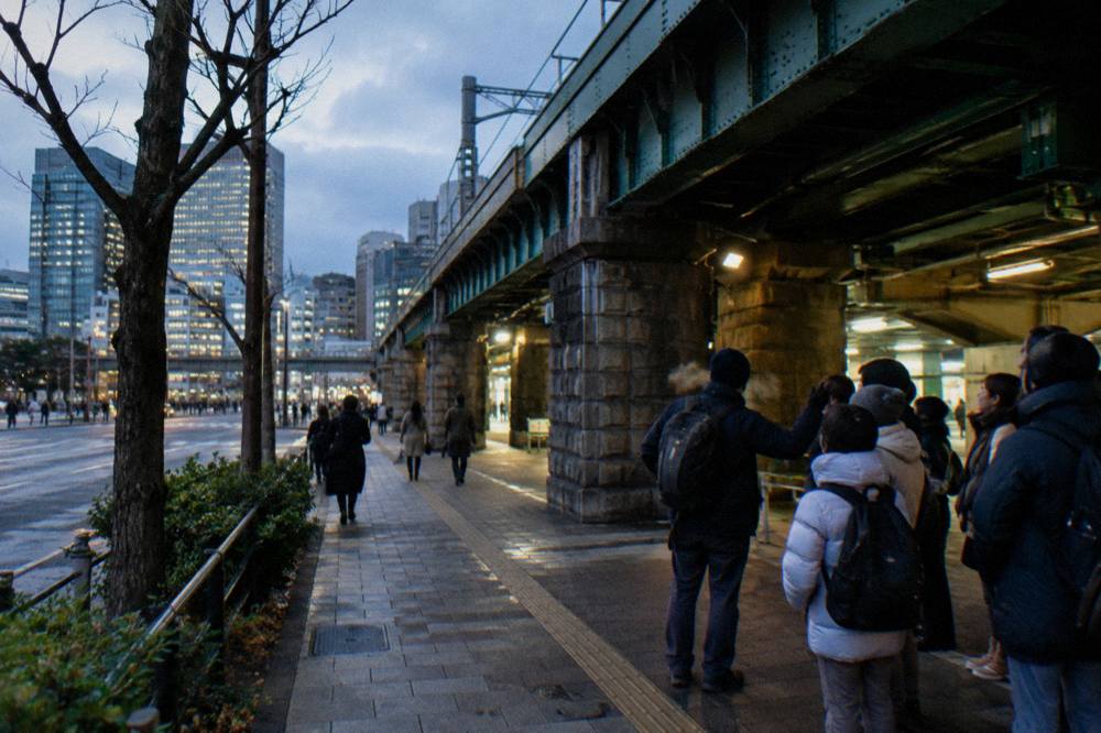 A small group gathered with a guide at the exit of a busy Tokyo train station in the early evening
