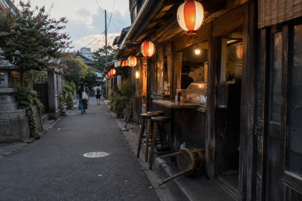A narrow pedestrian lane in Tokyo lined with small counters and hanging lanterns at dusk
