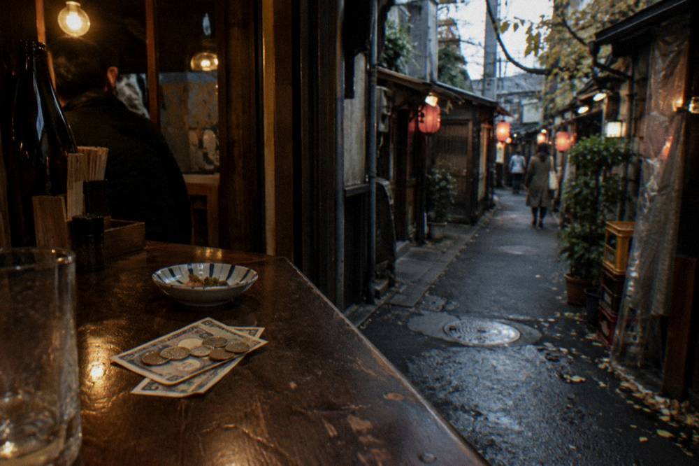 Japanese banknotes and coins resting on a wooden restaurant counter beside a small dish