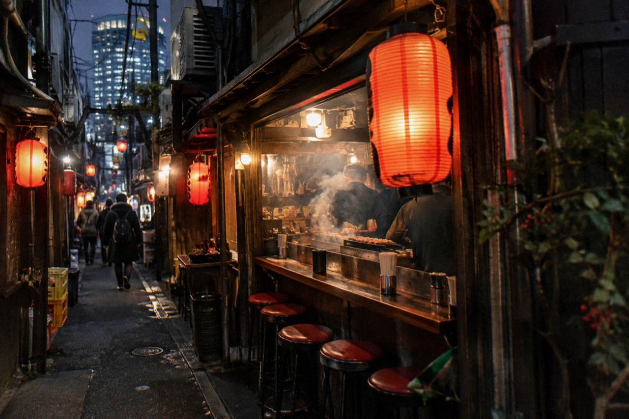 A narrow lantern-lit Tokyo alley with small restaurant signs and steam rising from a food stall