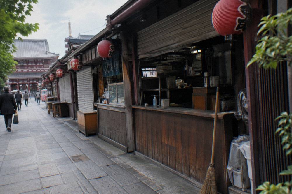 Row of small food stall fronts with red paper lanterns along a narrow Asakusa lane