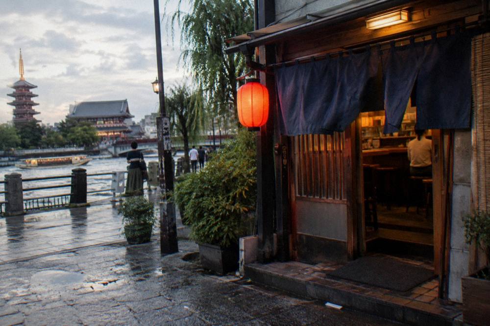 Small counter restaurant entrance with noren curtain and hand-written menu signs in Asakusa