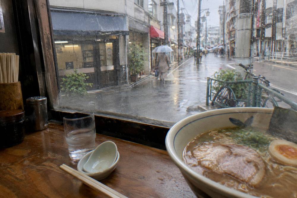 A bowl of ramen with sliced pork and egg beside chopsticks on a counter